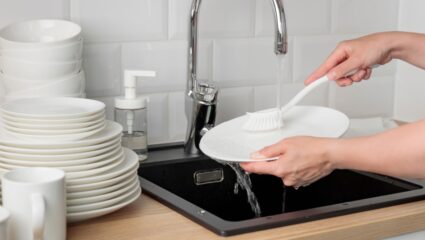 Iemand maakt haar vaat schoon met een afwasborstel.