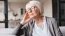 dementie-shutterstock_2115835502-1200×667 Een vrouw met dementie kijkt opzij, terwijl ze op de bank zit.