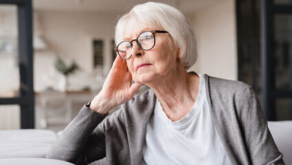 Een vrouw met dementie kijkt opzij, terwijl ze op de bank zit.