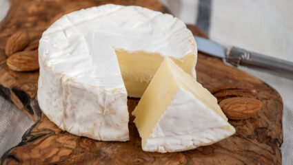 Een aangesneden ronde camembert op een houten plank.