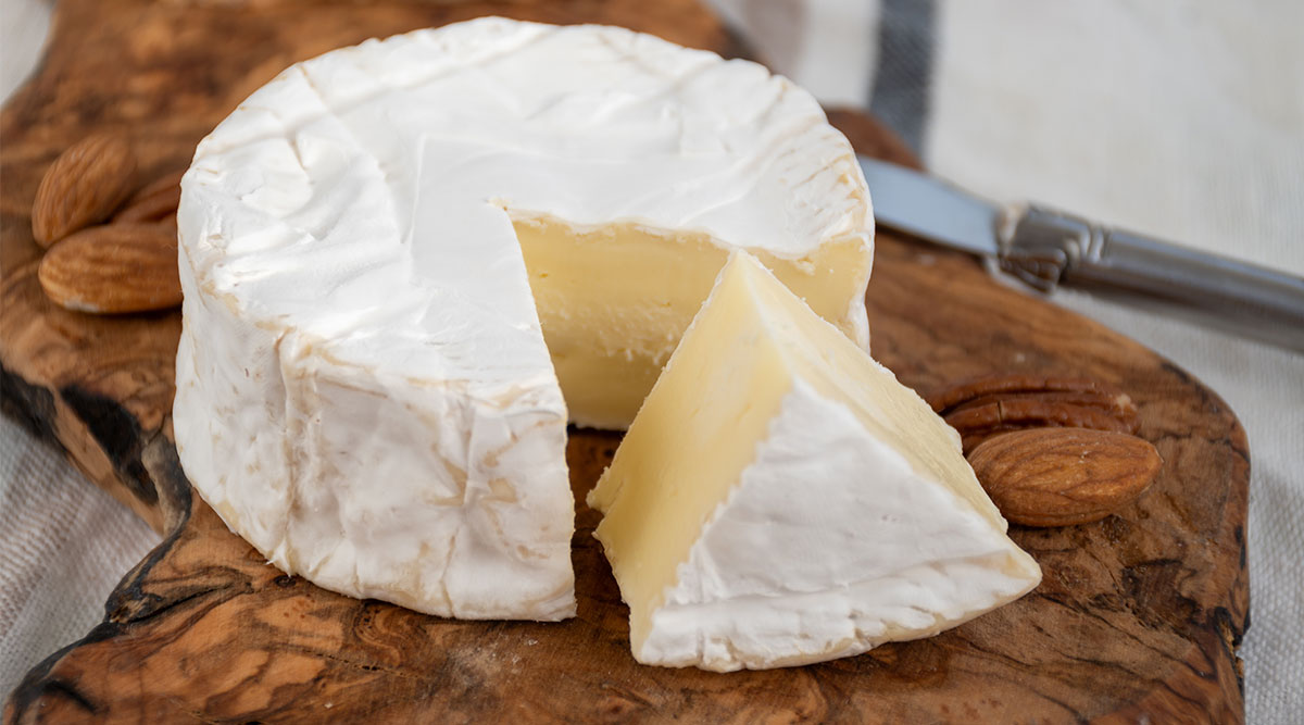 Een aangesneden ronde camembert op een houten plank.