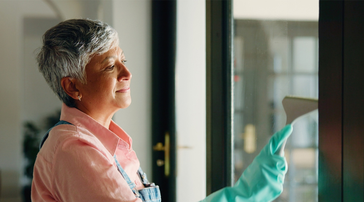 Een mevrouw maakt de ramen schoon met een raamwisser.