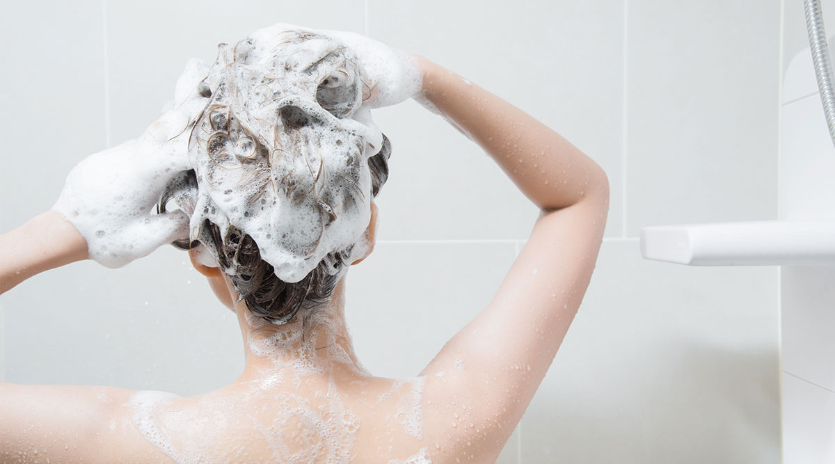 Vrouw staat onder de douche en wast haar haar met shampoo.