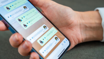 Een hand houdt een telefoon vast. Hierop zijn diverse spraakberichten in WhatsApp te zien.
