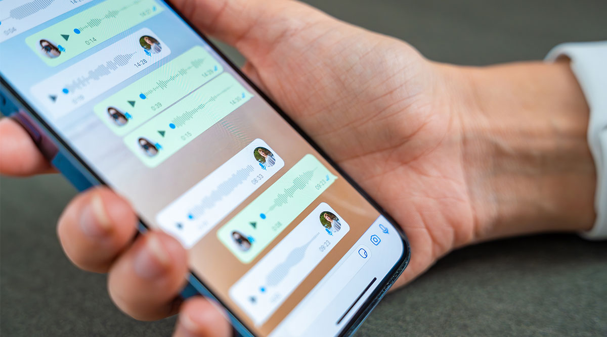 Een hand houdt een telefoon vast. Hierop zijn diverse spraakberichten in WhatsApp te zien.