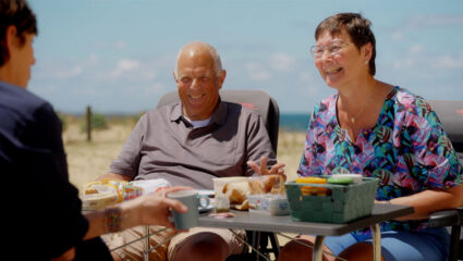 Martine van Os zit aan een campingtafel met Bram en José uit We zijn er Bijna!