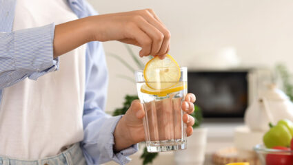 Een vrouw houdt een glas citroenwater vast.