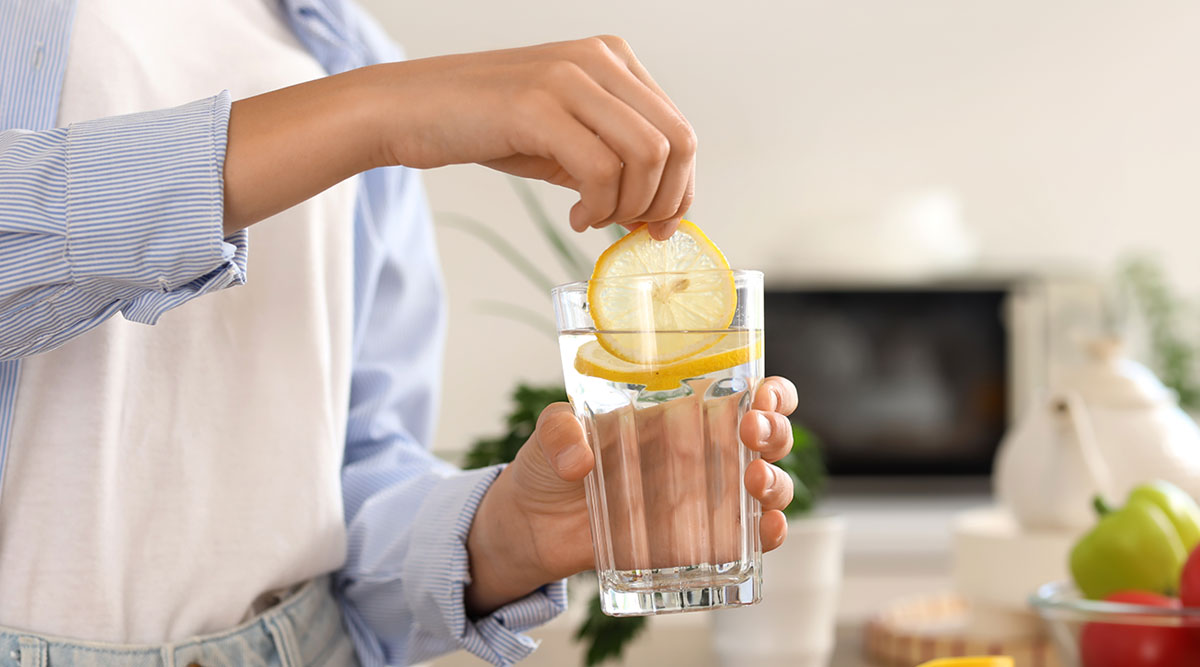 Een vrouw houdt een glas citroenwater vast.