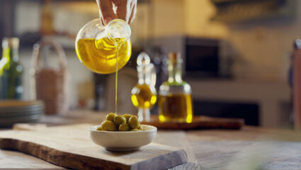 Olijfolie wordt over een schaaltje olijven gegoten.