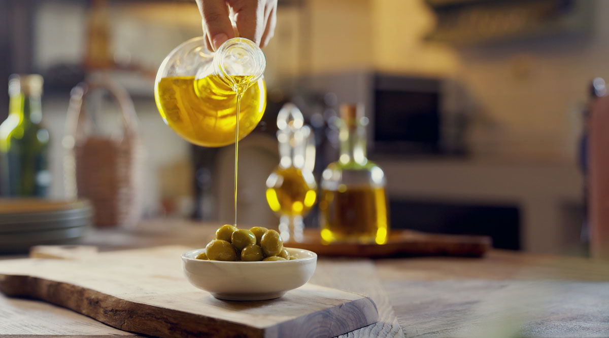 Olijfolie wordt over een schaaltje olijven gegoten.