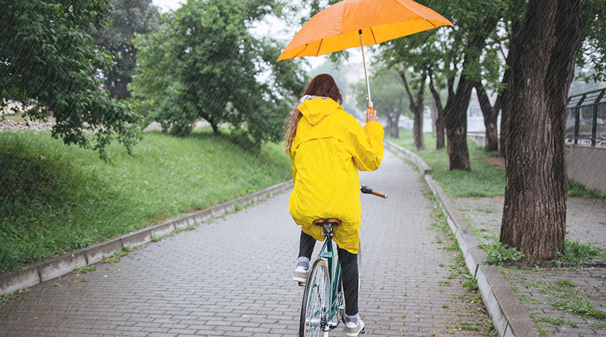Een vrouw fietst door de regen met een paraplu in haar hand.