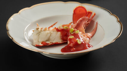 Kreeft met ketchupsaus op een wit bord met gouden rand en een zwarte achtergrond.