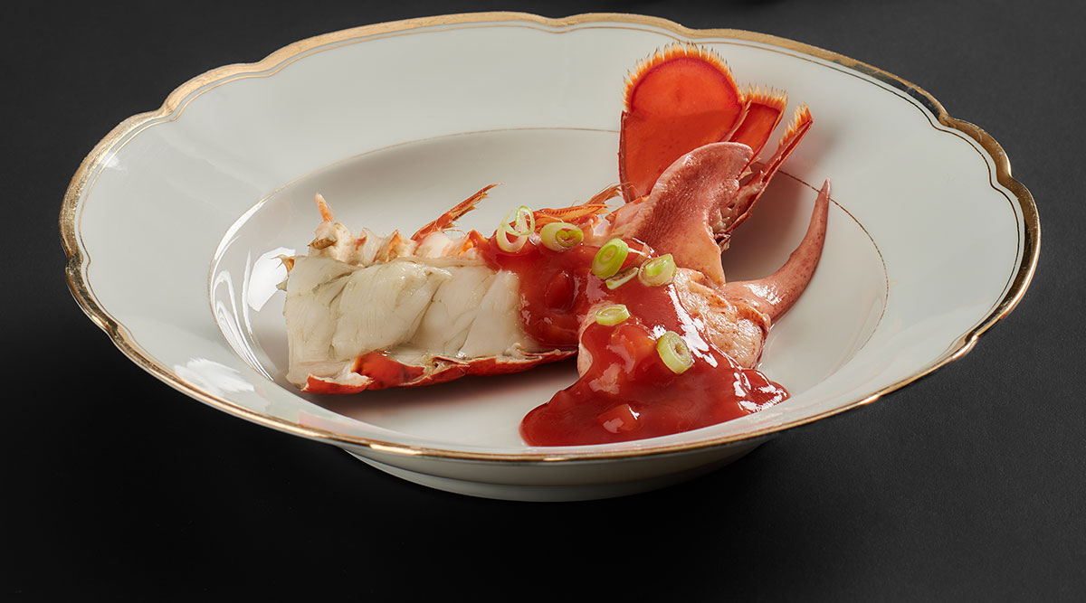 Kreeft met ketchupsaus op een wit bord met gouden rand en een zwarte achtergrond.