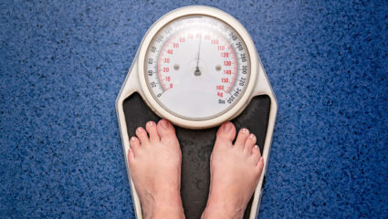 Beeld van een persoon, waar alleen de voeten van zichtbaar zijn, op een weegschaal.