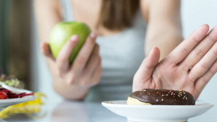 Vrouw wijst een donut af en eet liever een appel.