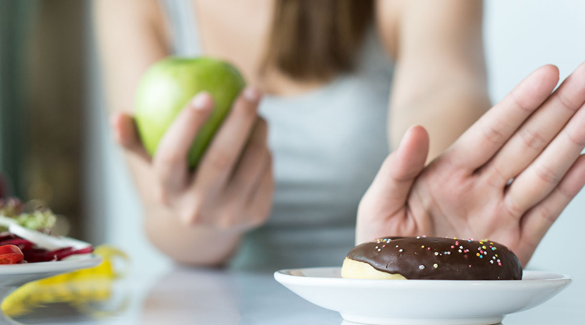 Vrouw wijst een donut af en eet liever een appel.