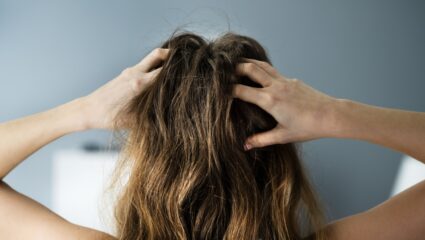 Een vrouw zit aan haar hoofdhuid omdat ze haarpijn heeft.