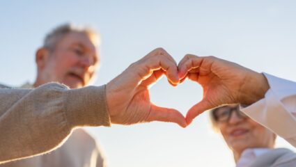 Een ouder koppel maakt een hart met hun handen.