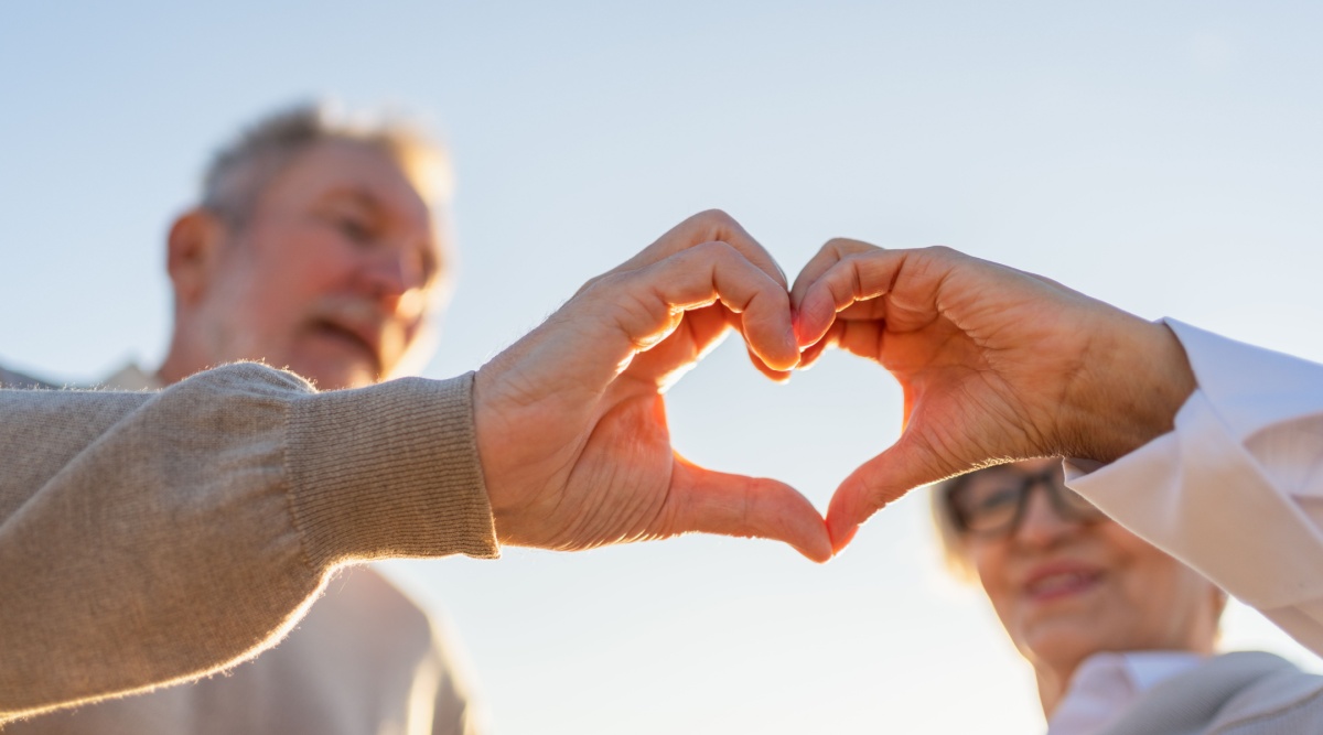 Een ouder koppel maakt een hart met hun handen.