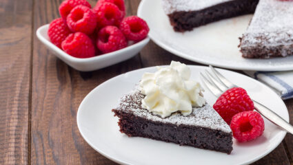 Zweedse kladdkaka taart op een wit bord met frambozen ernaast.
