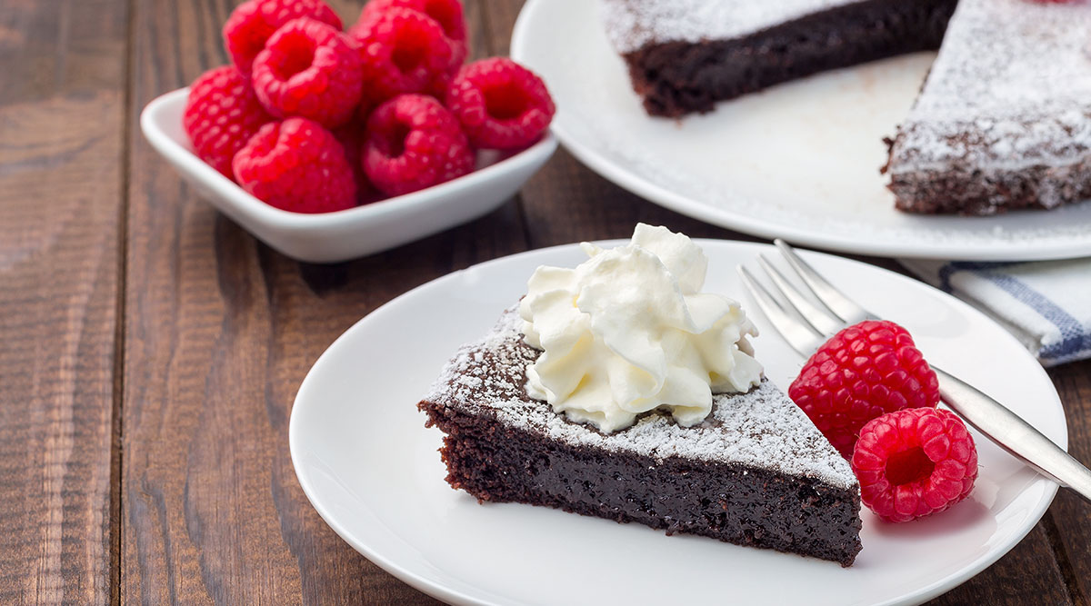 Zweedse kladdkaka taart op een wit bord met frambozen ernaast.