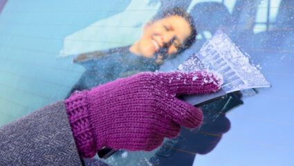 Mevrouw krabt de autoruit waar ijs op zit.