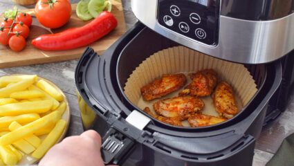 Een airfryer met gebakken kip in het mandje en friet