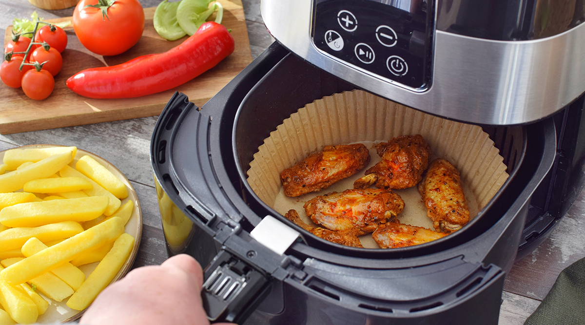 Een airfryer met gebakken kip in het mandje en friet