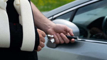 Iemand gaat met een arm in de mitella de auto in.