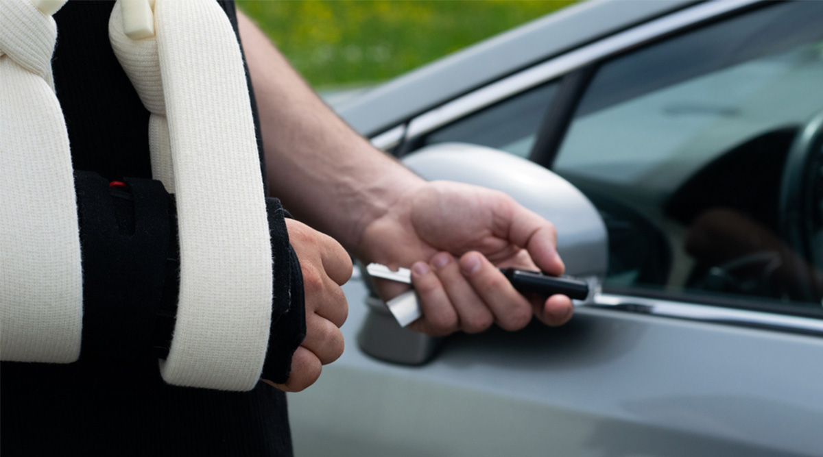 Iemand gaat met een arm in de mitella de auto in.