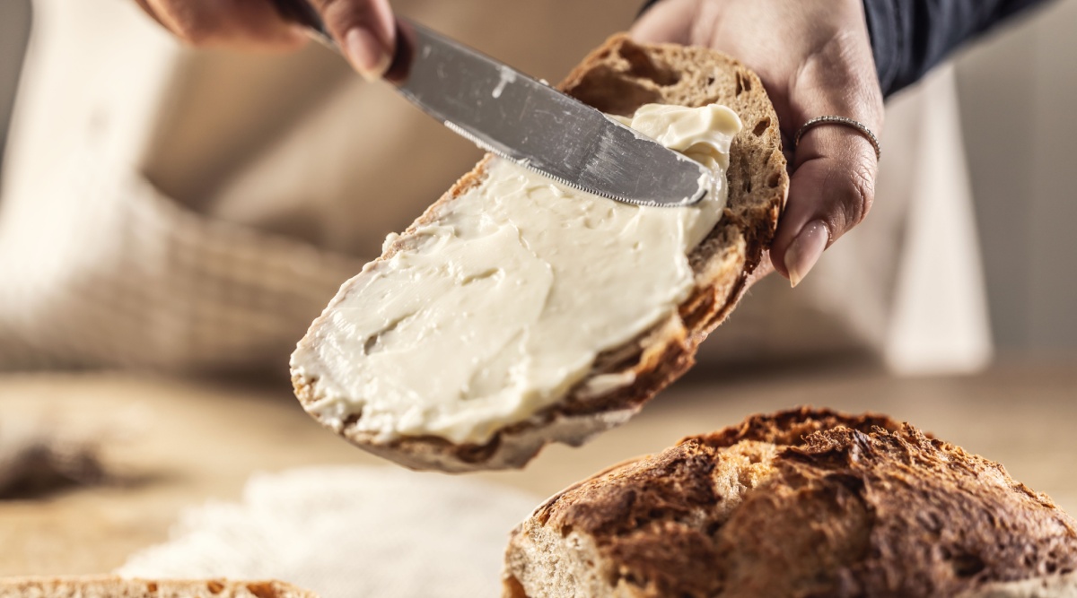 Iemand smeert smeerkaas op haar brood.