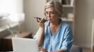Vrouw-Bril-Bellen-Laptop-Shutterstock_2516791129-1200×667 Vrouw met bril en kort grijs haar achter laptop met telefoon in haar hand