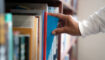 Iemand pakt een boek uit de kast.
