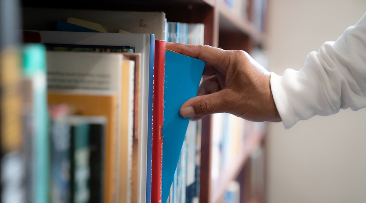 Iemand pakt een boek uit de kast.