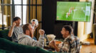 Drie mannen zitten op de bank het EK voetbal te kijken met hapjes.