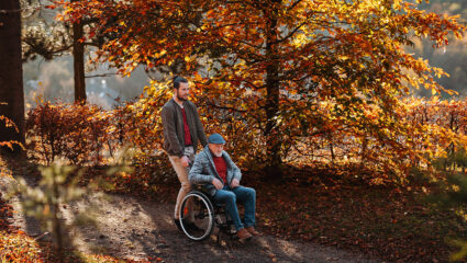 Een man in een rolstoel maakt een wandeling met zijn kleinzoon, in een herfstachtig bos.