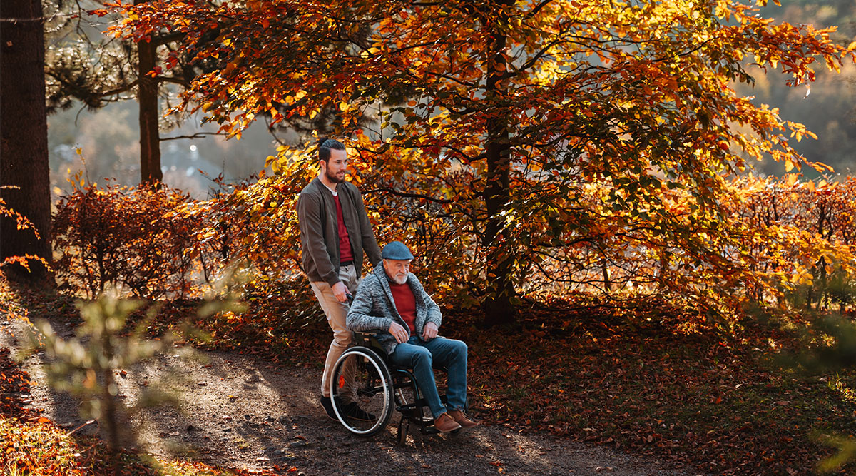 Een man in een rolstoel maakt een wandeling met zijn kleinzoon, in een herfstachtig bos.