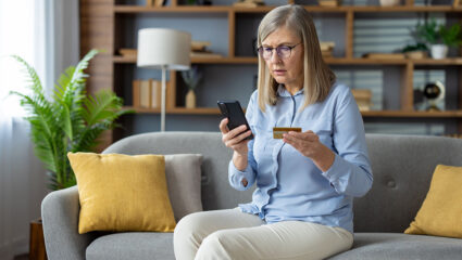 Een vrouw zit met haar telefoon en bankpas in de hand, in het kader van online fraude.