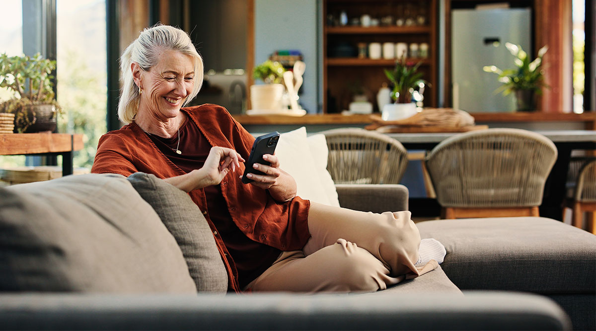 Een vrouw zit op de bank met haar telefoon in de hand. Ze is bezig om haar beveiliging in WhatsApp aan te passen.