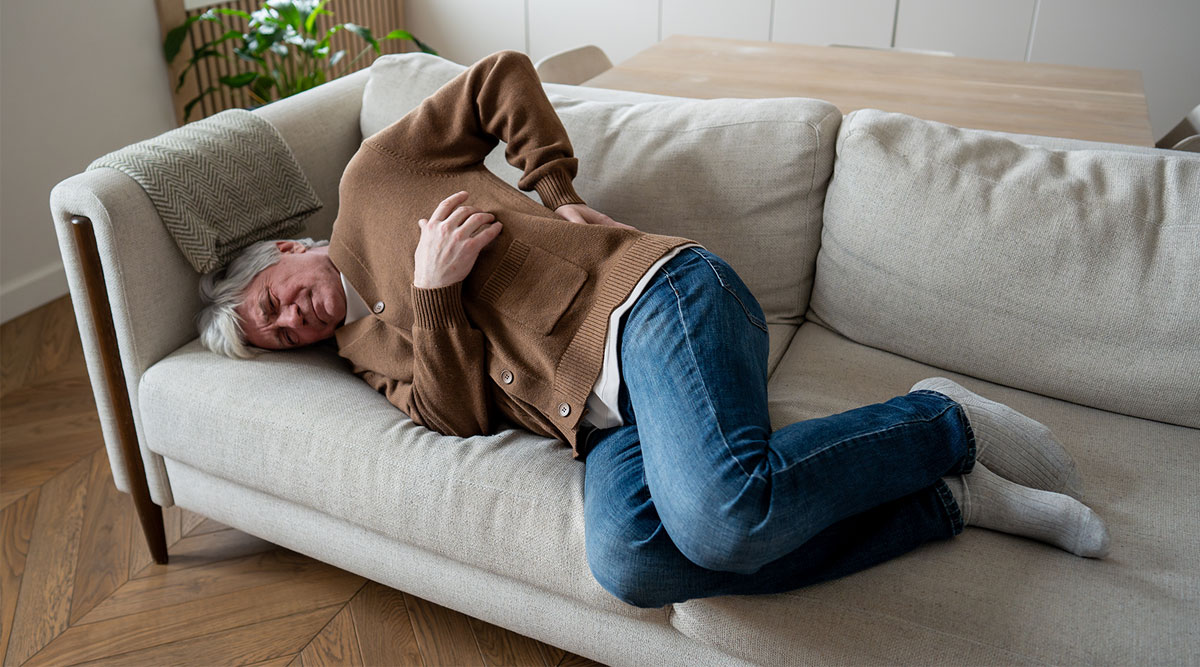 Een oudere man ligt met rugpijn op de bank.