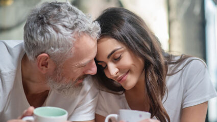 Oudere man en jongere vrouw liggen liefdevol tegen elkaar aan.