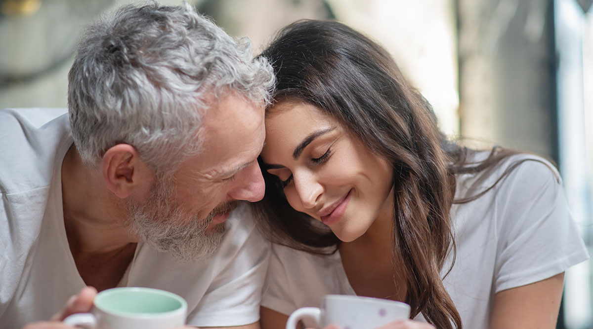 Oudere man en jongere vrouw liggen liefdevol tegen elkaar aan.