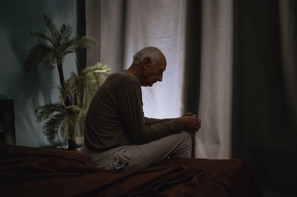 Man zit op de rand van zijn bed in een donkere slaapkamer