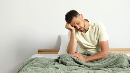 Een man met slaaptekort zit op bed en oogt vermoeid.