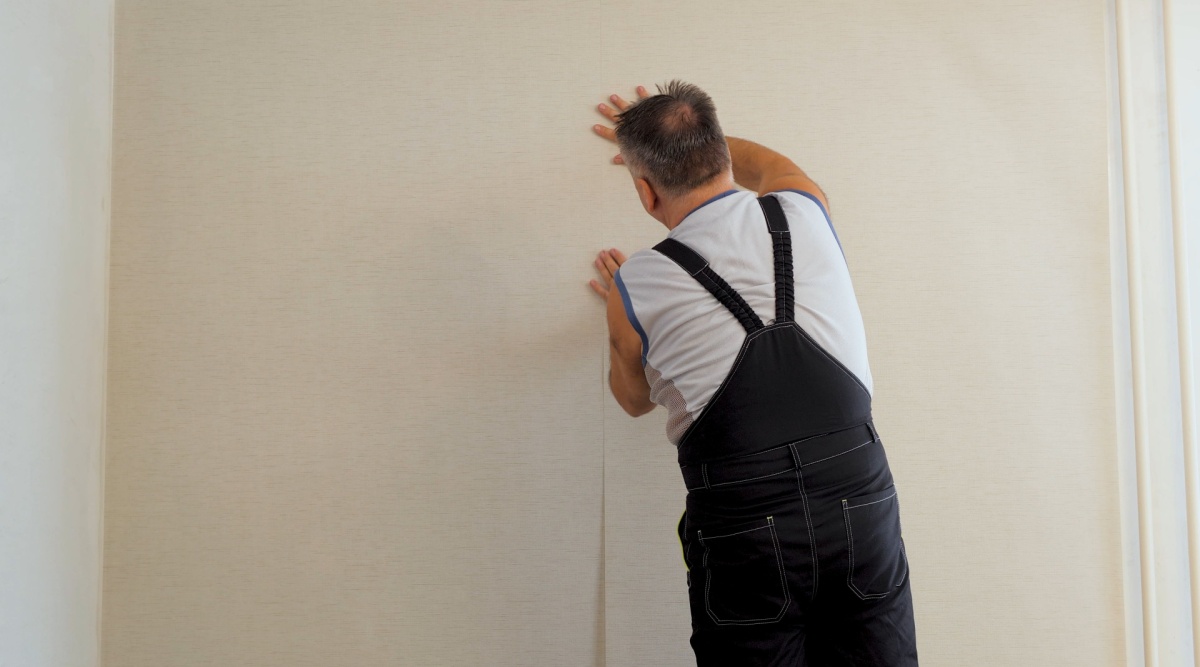 Een man is de muur aan het behangen.