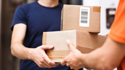 Een (post)bezorger geeft 2 pakketten aan iemand.