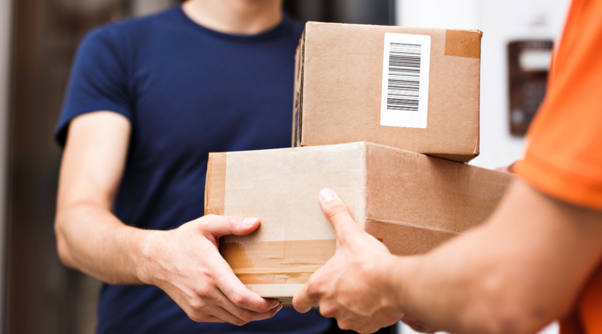 Een (post)bezorger geeft 2 pakketten aan iemand.