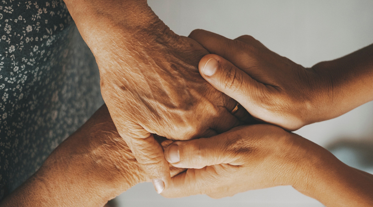 Een mantelzorger houdt de hand van diens partner vast.