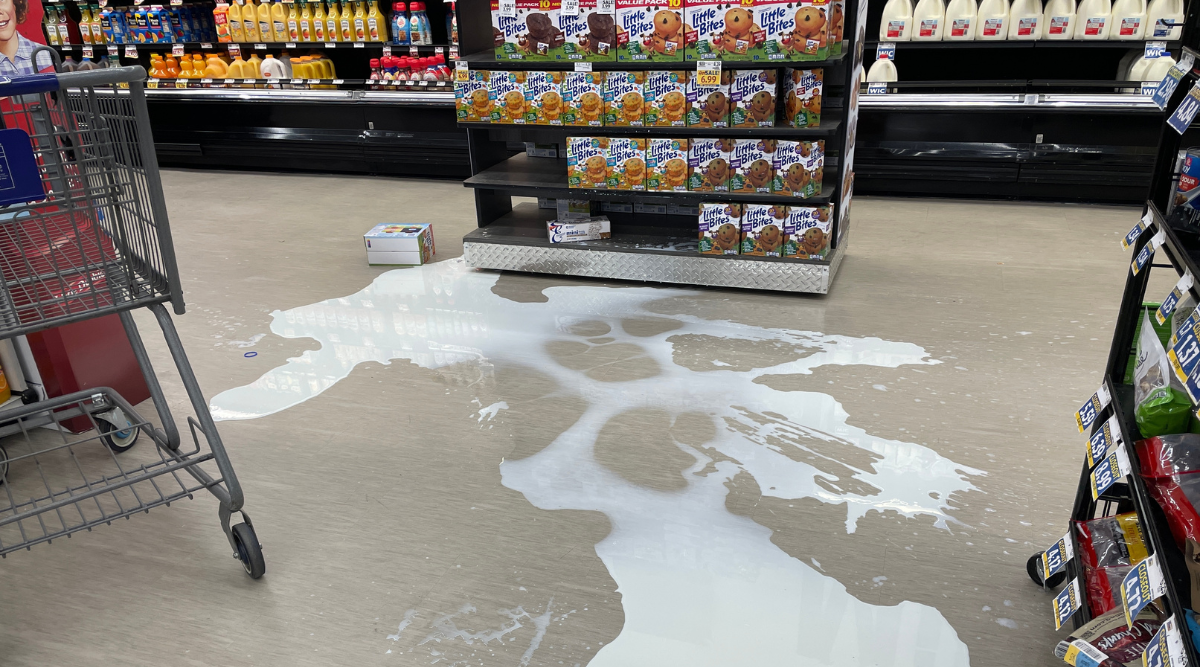 Kapot gevallen pak melk in supermarkt met grote melkvlek op de grond
